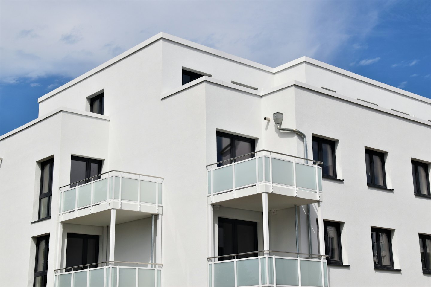 Modernes Wohnhaus mit Balkonen vor blauem Himmel.