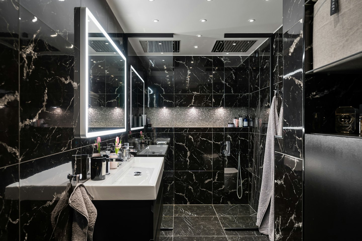 Modernes Badezimmer mit Marmorfliesen und beleuchteten Spiegeln.